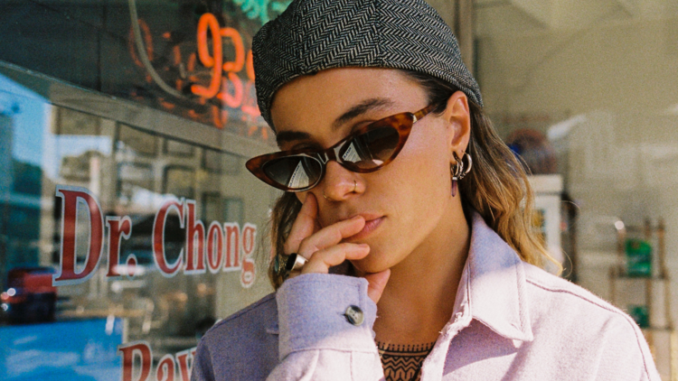 Singer and multi-instrumentalist Tash Sultana wearing a grey cap and brown cat eye sunglasses.