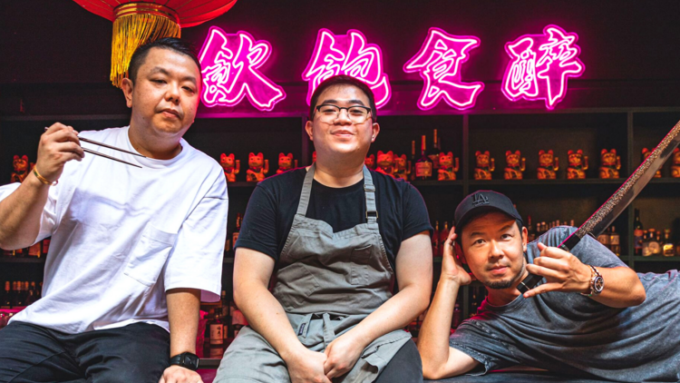 Three chefs smiling in front of neon chinese characters