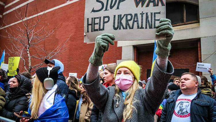 A group of protestors, one of whom is holding a sign that reads Stop War Help Ukraine.