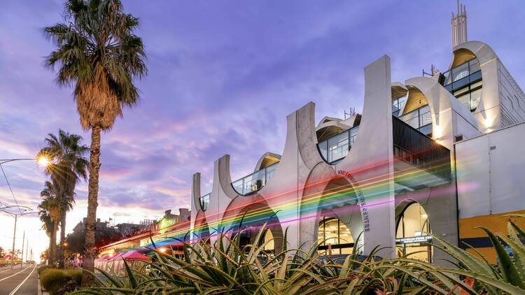 The exterior of the Victorian Pride Centre with beams of rainbow-coloured light shooting across.