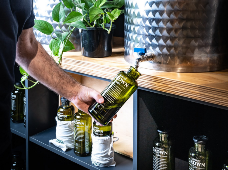 A person refilling a green gin bottle from a vat