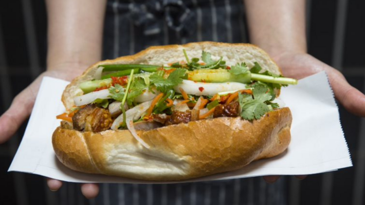 Someone in a chefs apron holds out a banh mi