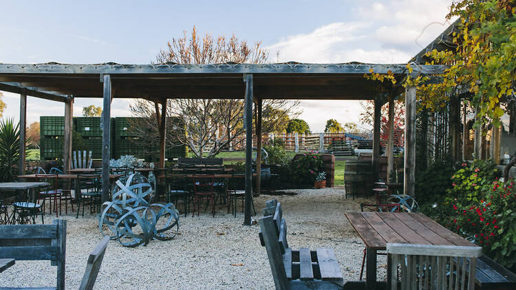Flynns Winery: a rustic winery cellar door with heaps of wooden tables and chairs and metal sculptures on a lawn.