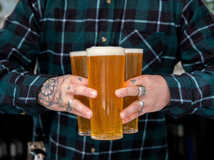 A man holding three schooners of beer in his hands.