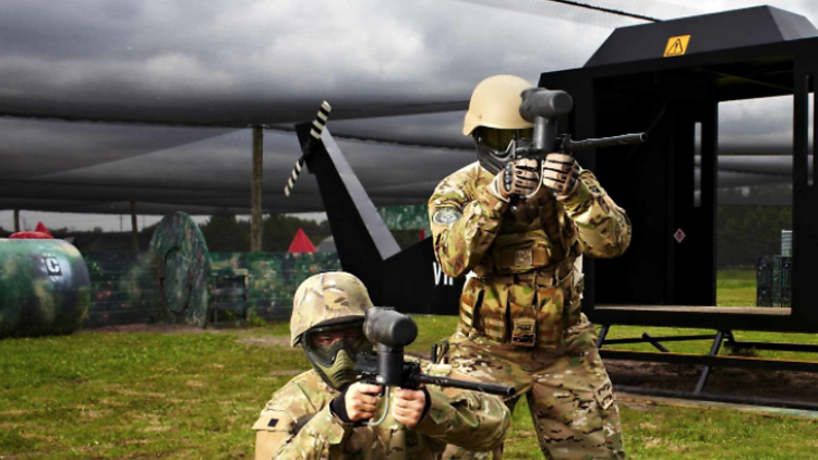 Two men in full tactical gear standing in a paintball field.