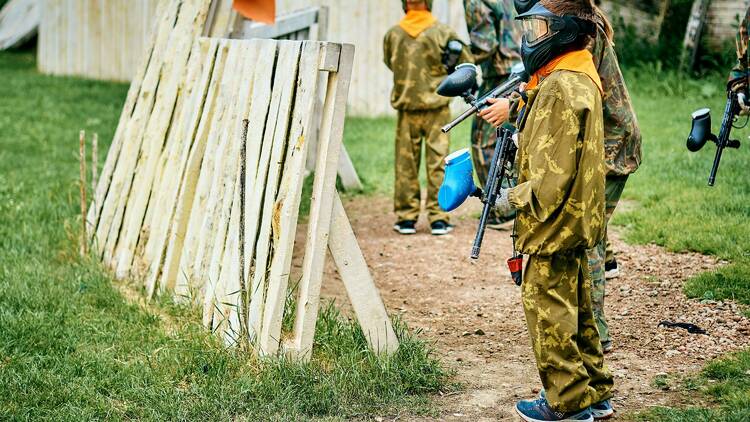 Kids standing behind a barrier while playing paintball. 