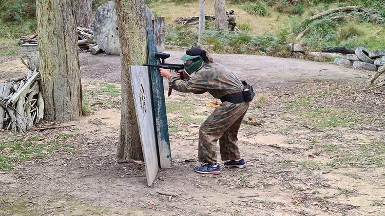 A person in tactical gear hiding at a paintball field.