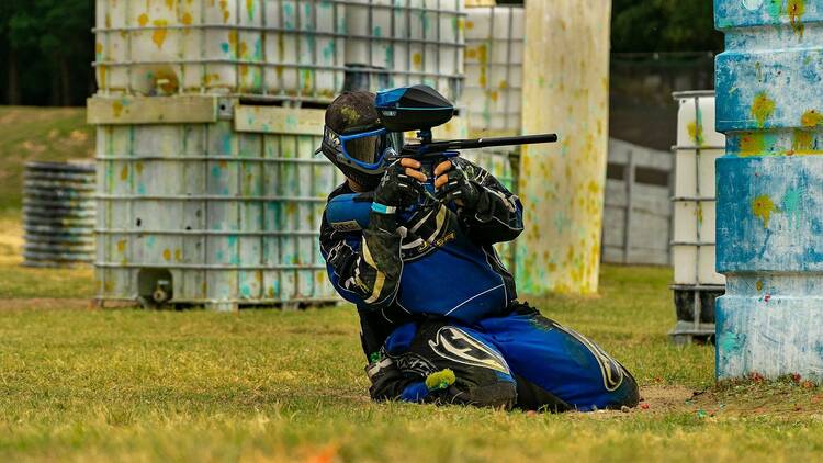 A person on their knees wearing tactical gear and wielding a paintball gun.