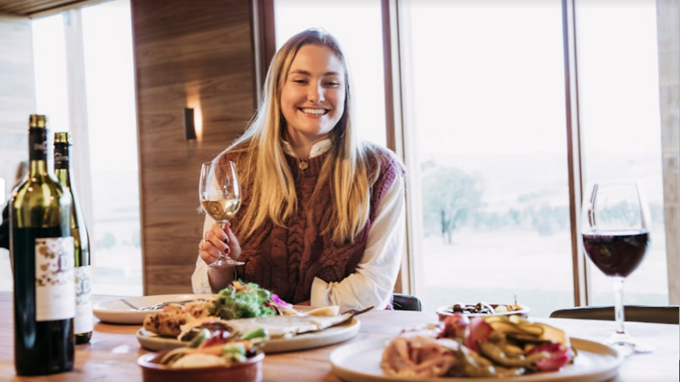 A woman holding a glass of wine and sitting at a table with charcuterie.