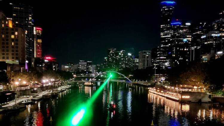 A green laser beam shoots along the Yarra River at night in Melbourne