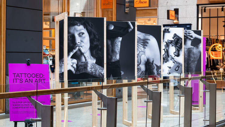 Five black and white portraits of people with tattoos on display in a shopping centre.