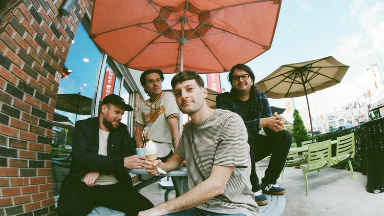 the members of the band Pup sitting at an outside table under an umbrella.