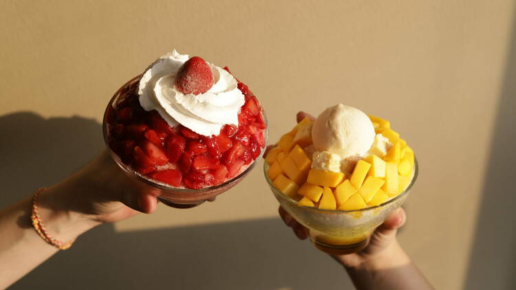 Two Korean bingsu shaved ice cream sundaes topped with strawberry and mango.