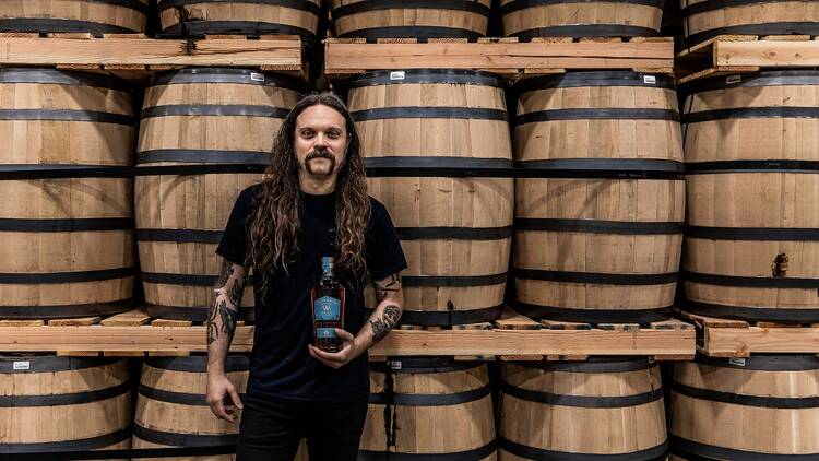 A man with long hair in front of a wall of whiskey barrels