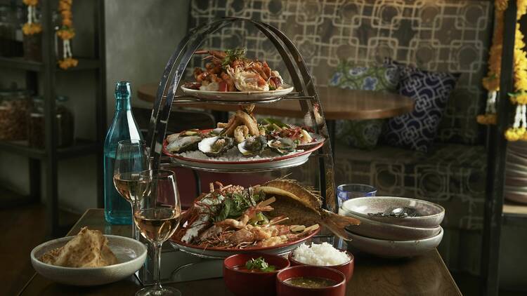 A three-tier seafood tower on a table with wine glasses and side dishes.