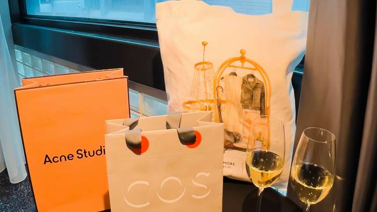 A variety of items on a table including glasses of wine, luggage tags and shopping bags.