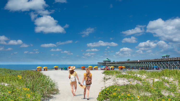 Teenage girls relaxing on  the beautiful beach, People enjoying summer vacation by the ocean.Girls walking on the beach.  Cloudy sky and pier in the background. Folly Beach, South Carolina USA. 