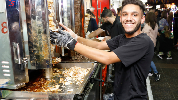 A super hot dude smiling and making a kebab. He is hot.