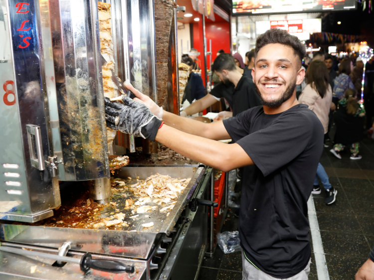 A super hot dude smiling and making a kebab. He is hot.