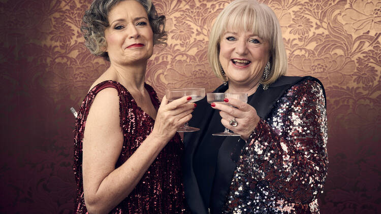 Judith Lucy and Denise Scott drink martinis in sparkly red outfits