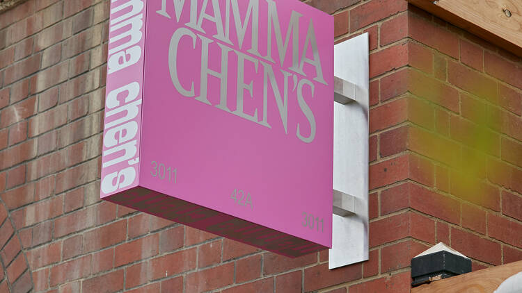 A pink sign on a brick building that reads Mamma Chen's.