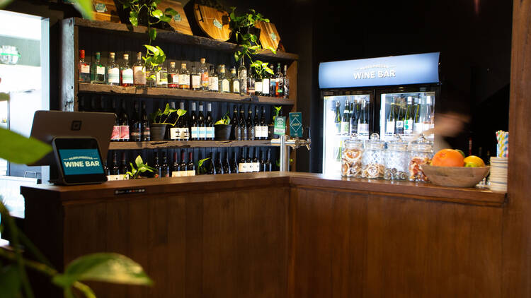 A wooden bar with shelves filled with spirits and wine bottles.