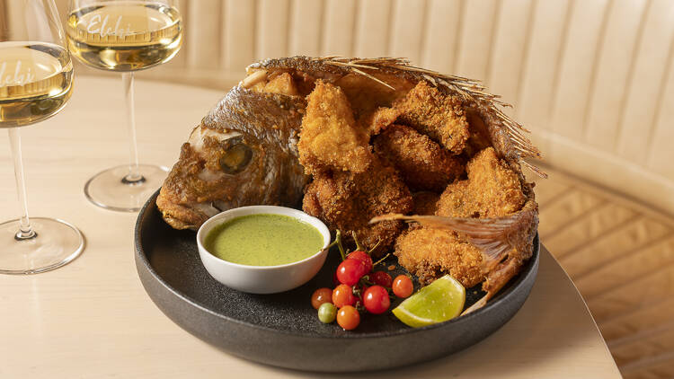 A whole fried fish served with a green sauce, and two glasses of wine.