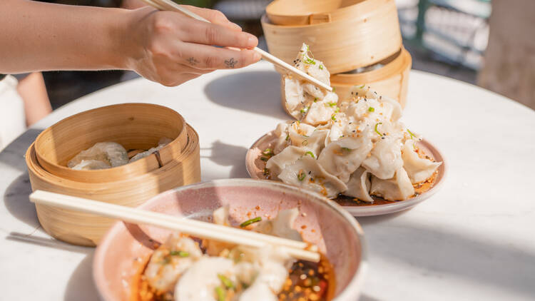 A person using chopsticks to grab dumplings off of a platter.