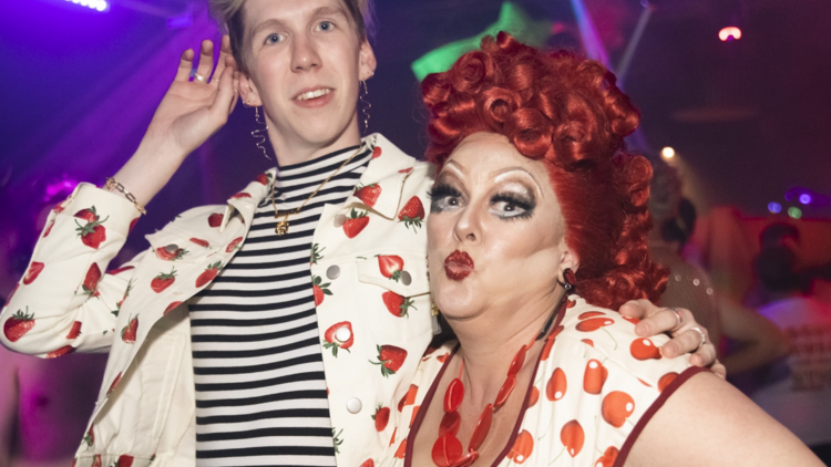 A drag queen and a blonde man wearing matching fruit-themed jackets.