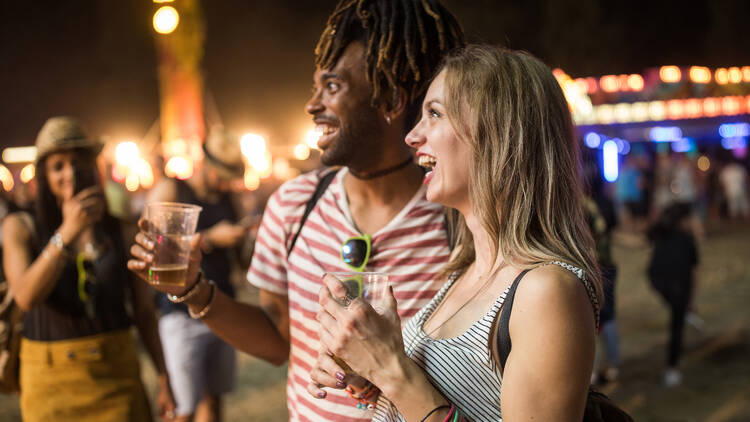 A dark-skinned man with dreadlocks and a pale blonde woman enjoy the festivities of a carnival.