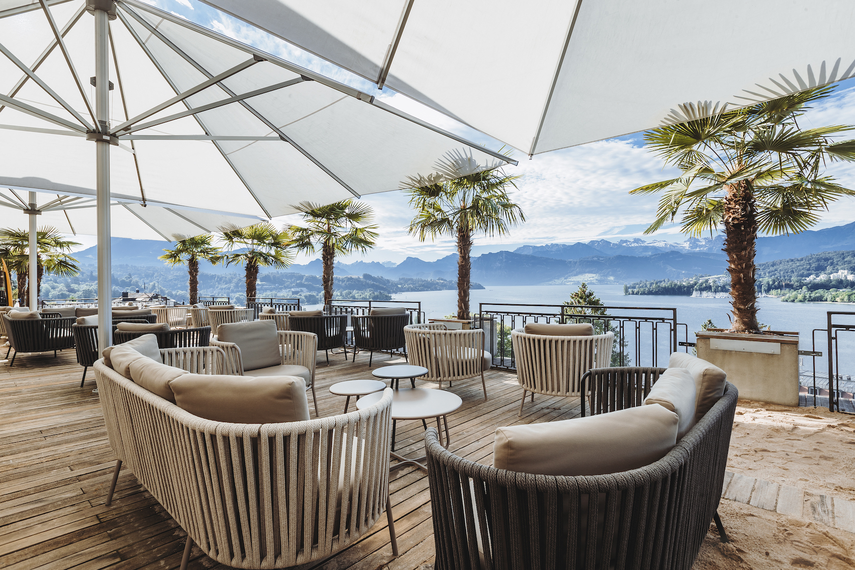 An outdoor terrace with palm trees and sofas at Art Deco Hotel Montana, Lucerne.