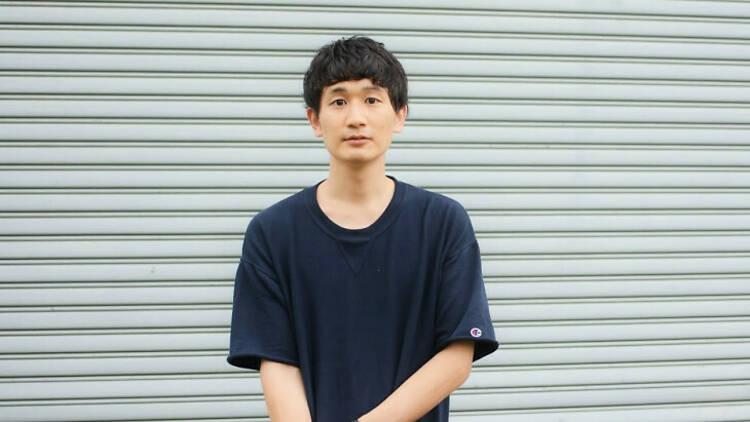 Comedian Takashi Wakasugi standing before a rolling garage door.