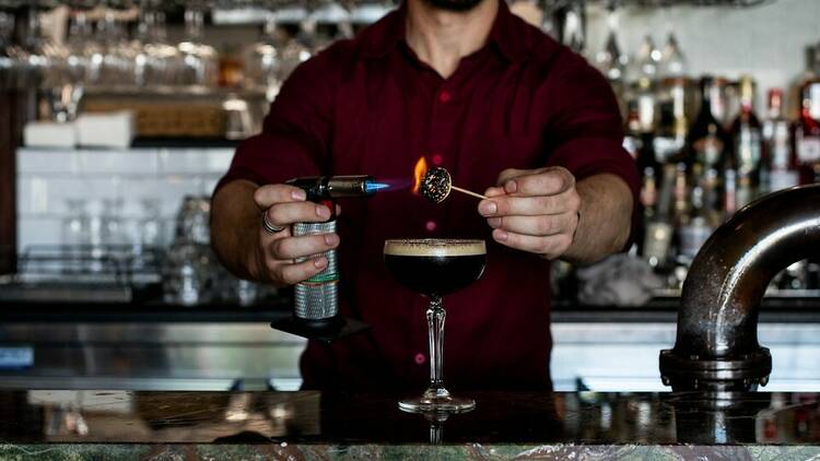 A bartender setting a marshmallow to flame atop an Espresso Martini.