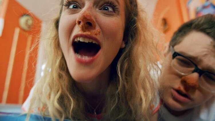 A still from the film Asshole Still; A close-up of a blonde woman with food on her face.
