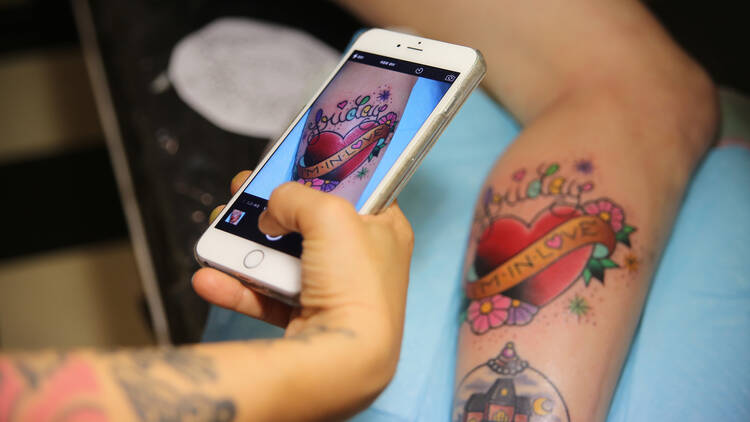 A person takes a photo on an iPhone of a colourful heart tattoo.