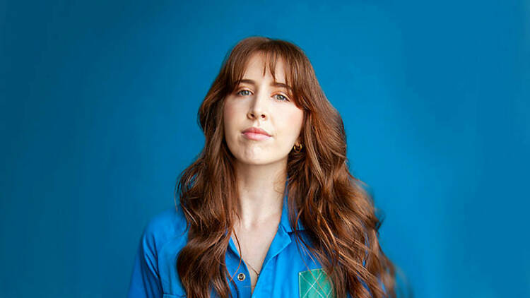 Comedian Lauren Bonner standing in front of a blue backdrop.