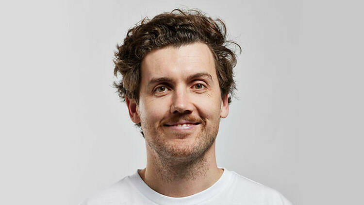 Comedian Daniel Connell in a white shirt in front of a white backdrop.