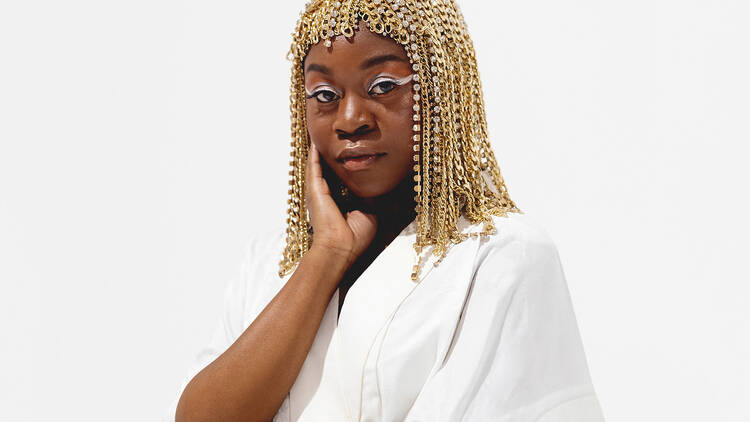 Sampa The Great in a white shirt and gold bedazzled wig