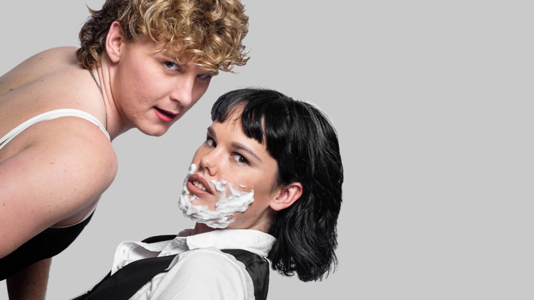 Jenna wears a white shirt and black vest and shaving cream on her face, Brendan lunges towards her in a swimsuit as they both stare down the camera