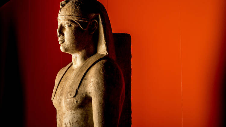 An ancient statue of a Greek boy in Egyptian dress on a red background