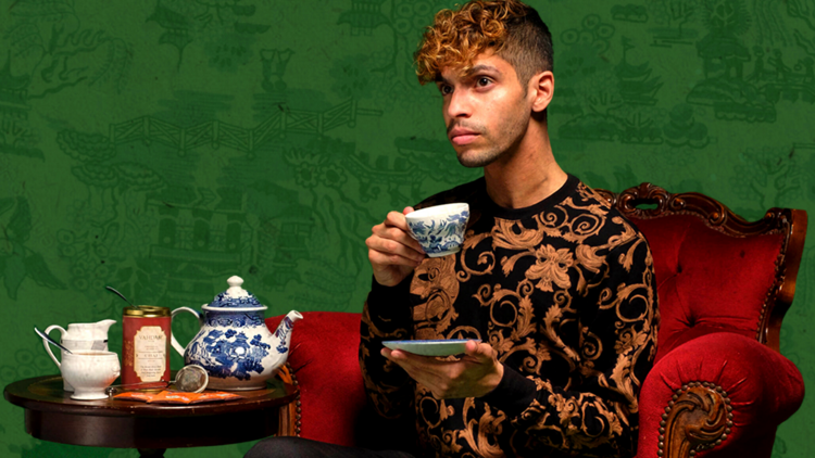 AJ Lamarque sits on a regal armchair drinking tea