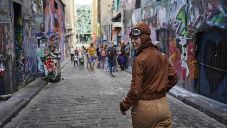 A woman dressed as a pilot walks down a laneway with street art.