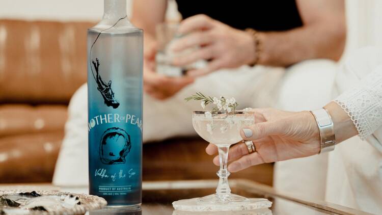 A bottle of Mother of Pearl vodka next to a cocktail garnished with a flower.