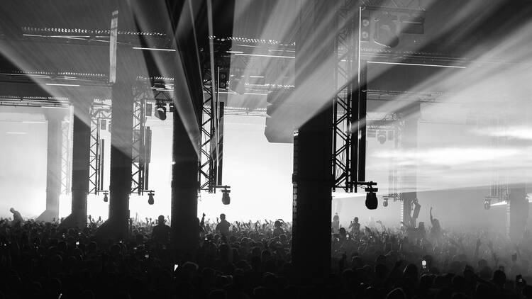 A mass of people inside a warehouse dancing in front of a brilliantly lit stage