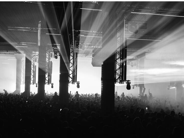 A mass of people inside a warehouse dancing in front of a brilliantly lit stage