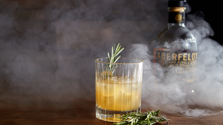 A cocktail in a tumbler with rosemary and smoke