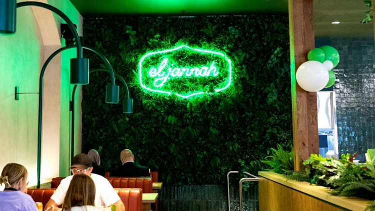 The interior of a charcoal chicken shop with a neon sign reading el jannah.