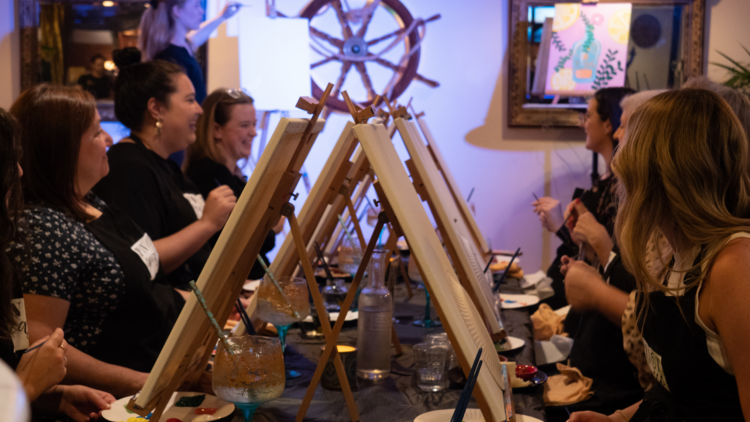 Mothers and children laugh while painting canvasses at Pinot Picasso's sip and sketch event