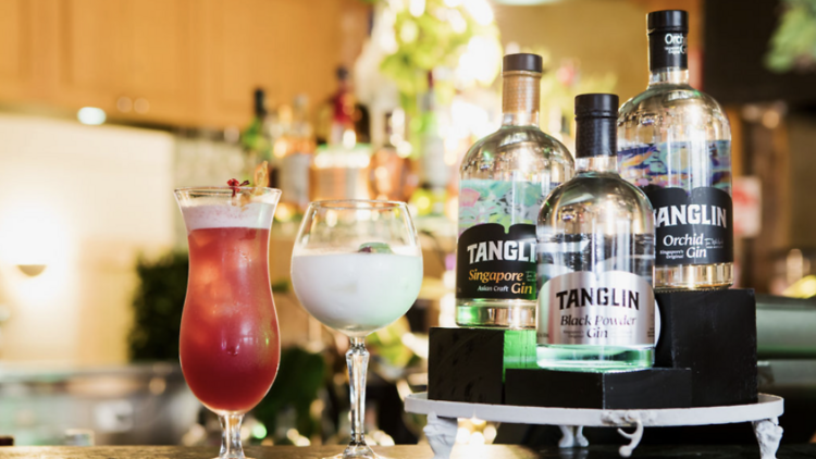 A range of Tanglin gin bottles next to two cocktails.