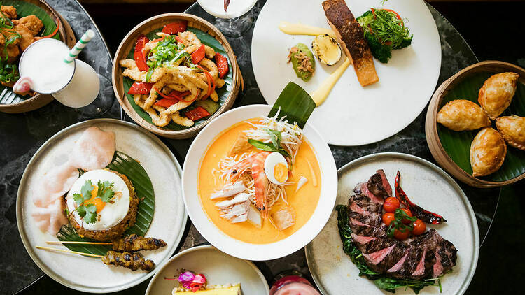 A range of Asian fare on a table including nasi goreng, a wagyu steak and soup.
